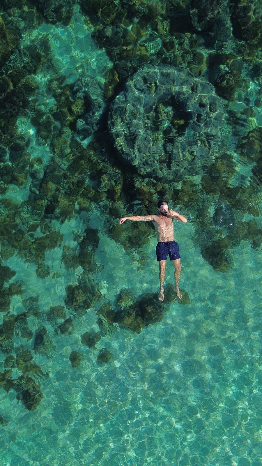 Swim Snorkel – man arms spread floating over dark reef (Real photo from a KEXI trip)
